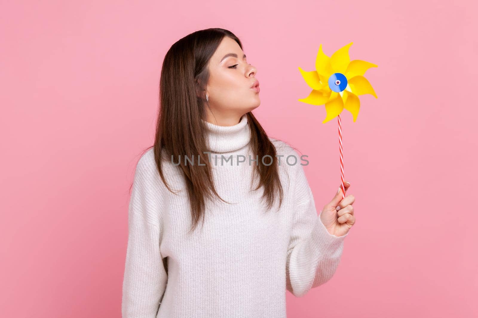 Portrait of carefree brunette woman blowing at paper windmill, playing with pinwheel toy on stick. by Khosro1