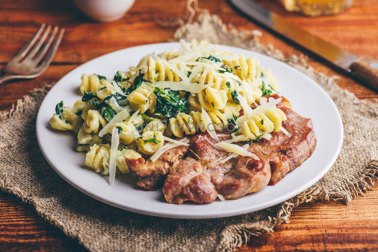 Pork Steak and Creamy Spinach Pasta Garnished with Parmesan Cheese on White Plate