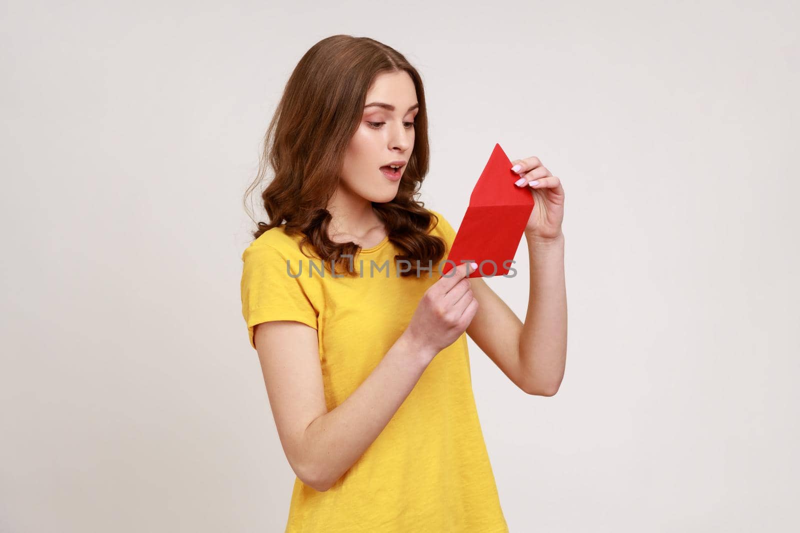 Side view of amazed young woman in yellow casual T-shirt opening envelope and reading letter, with surprised expression, got unexpected pleasant news. by Khosro1