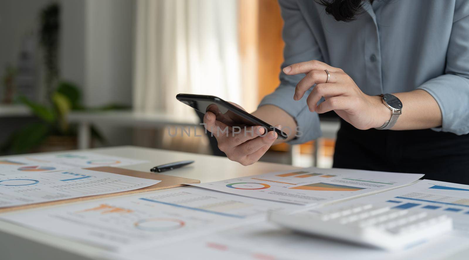 Close up hand of business woman or accountant using mobile phone and working for financaial chart graph report. by nateemee