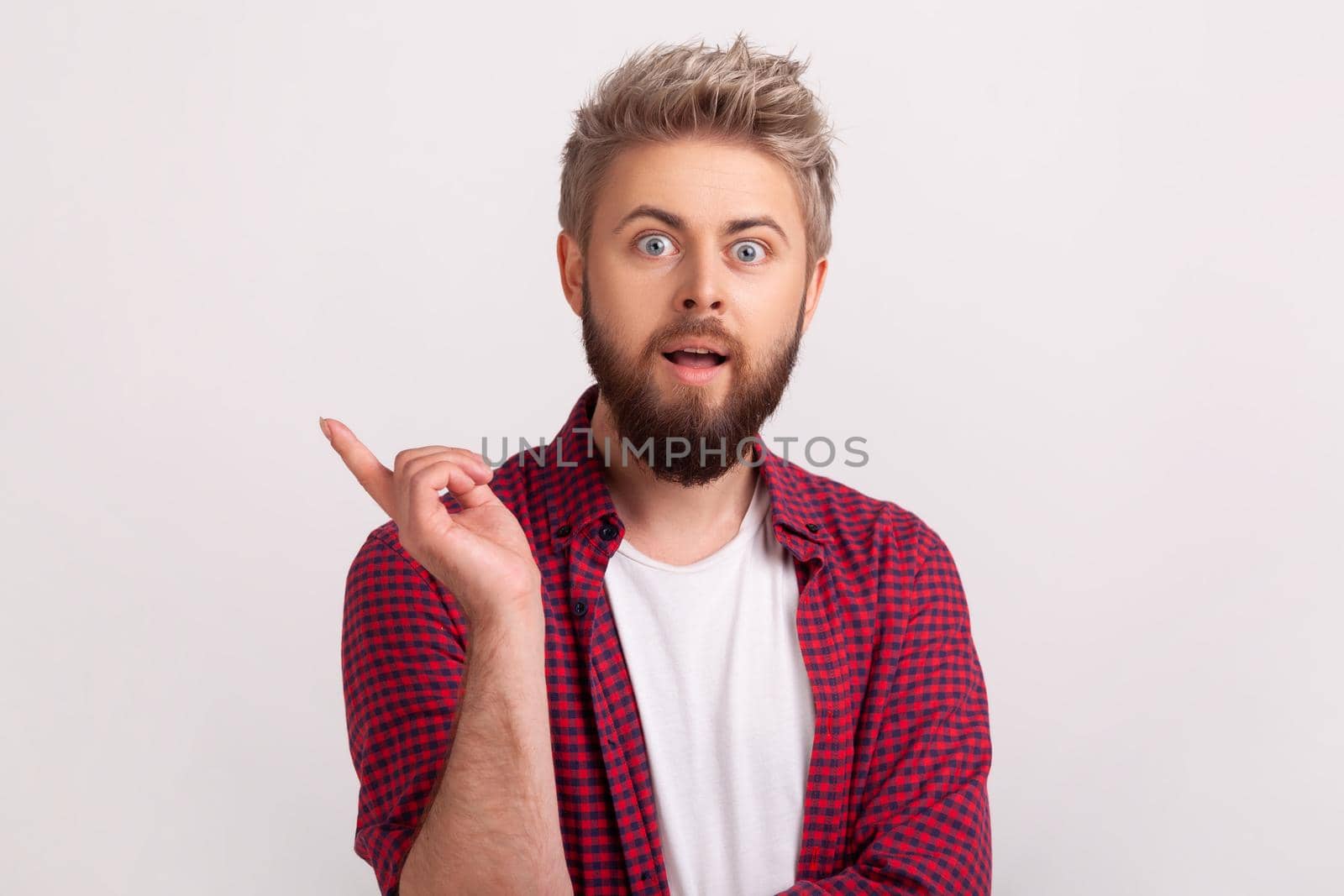 Portrait of inspired bearded man with opened mouth pointing finger up and looking at camera, having good idea, inspiration. Indoor studio shot isolated on gray background