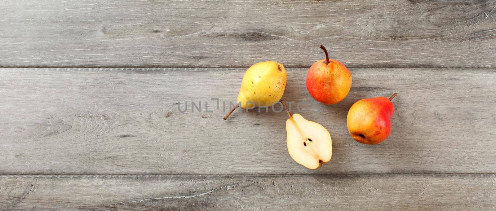 Four ripe pears, one cut in half, table top view, wide banner format.