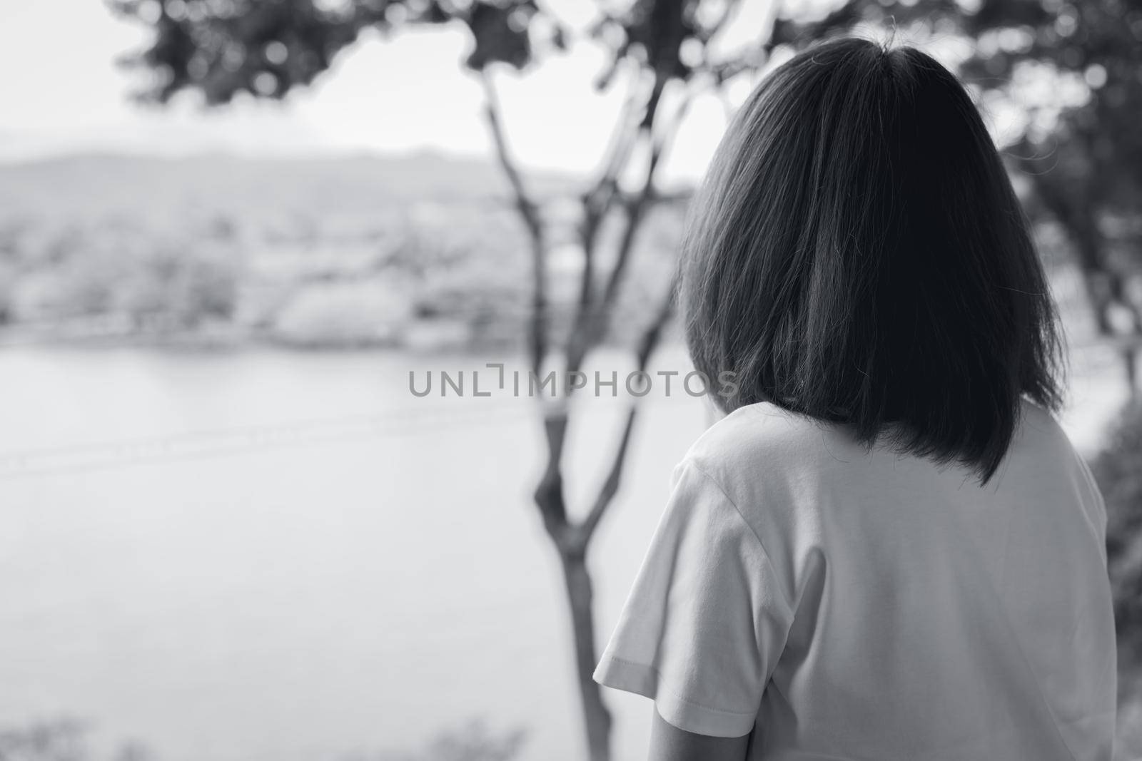 Back view of sad Asian woman in the park look the view of lake. Depressed woman. Mental health concept. Worry and anxiety woman. Unhappy life. Alone and lonely person. Black and white photography. by Fahroni