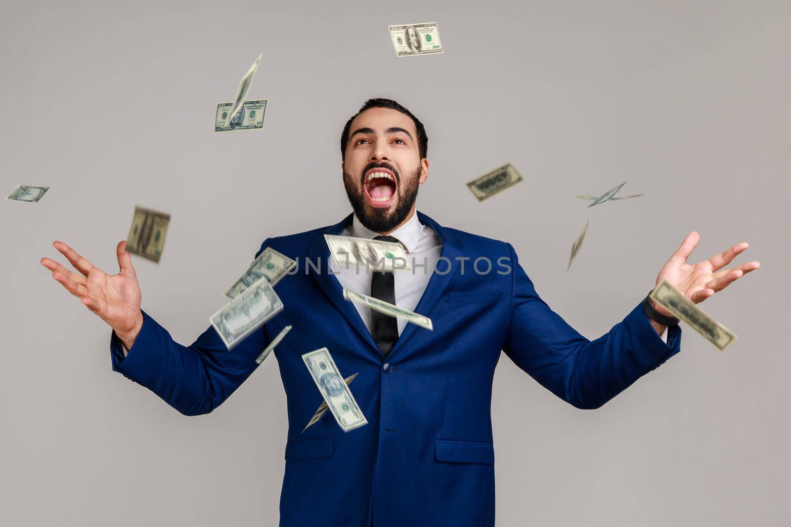 Rich lucky bearded man screaming yes i did it, joyful reacting to success, victory, money rain falling from up, celebrating, wearing official style suit. Indoor studio shot isolated on gray background