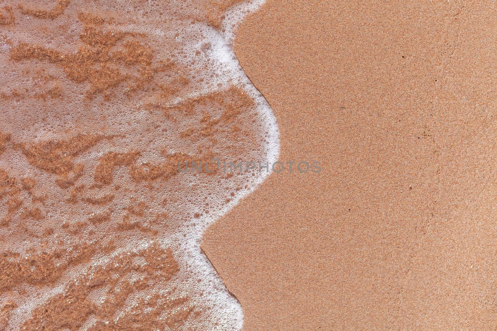 A soft wave runs on a sandy shore on a summer day. Empty space can be used as background for display or montage your top view products.