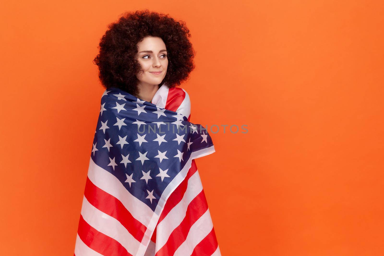 Calm dreamy woman with Afro hairstyle wearing green casual style sweater standing wrapped in USA flag, looking away, human rights. by Khosro1