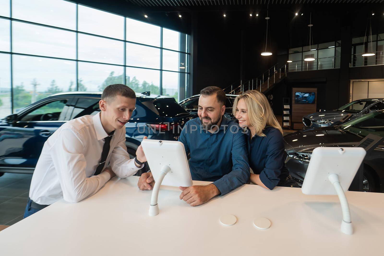 Caucasian married couple chooses a car in a car dealership on digital tablets