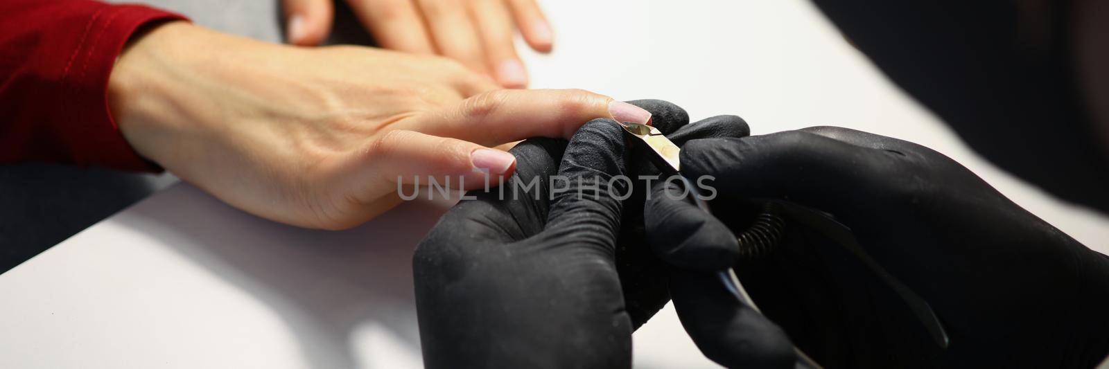 Close-up of nail master cutting off cuticle on clients hands with special equipment. Professional work in black gloves. Beauty industry, wellness concept