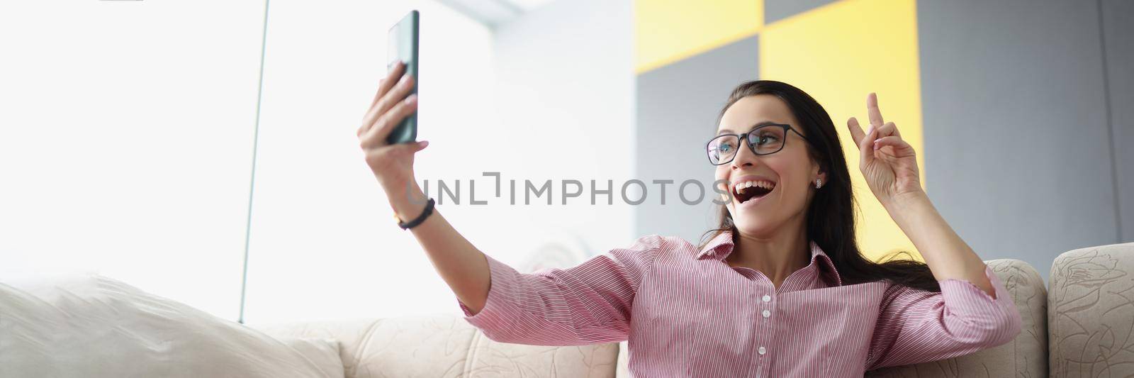 Pretty young female show peace sign and take selfie on smartphone by kuprevich