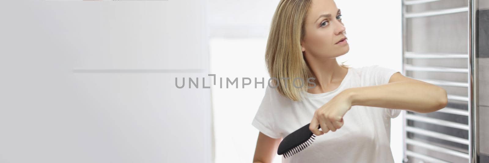 Portrait of young blonde woman looking in mirror and brushing hair in bathroom, no makeup, morning routine, natural beauty. Good morning, wellness concept