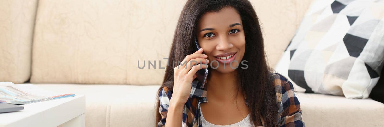 Portrait of lovely afroamerican girl talk on smartphone with friend, cute latin female at home on floor. Discuss funny moments, happy to hear. Call concept