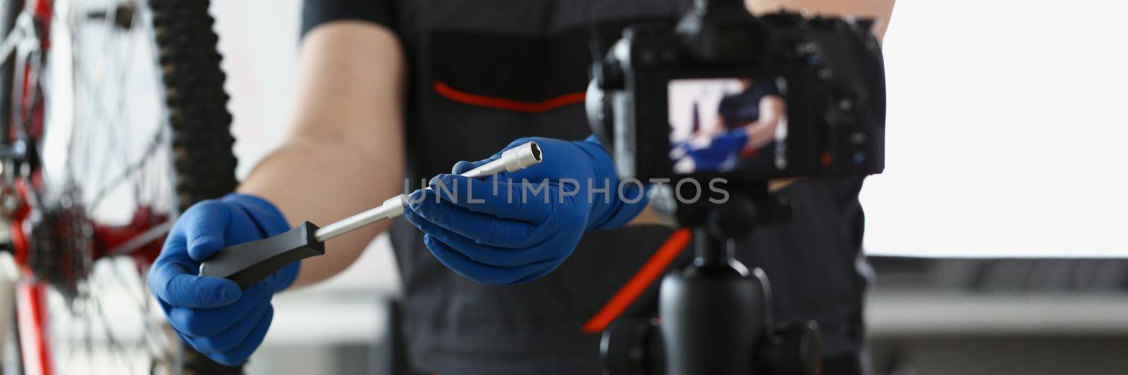 Blogger mechanic fix bicycle in workshop, busy young worker in shirt and gloves by kuprevich