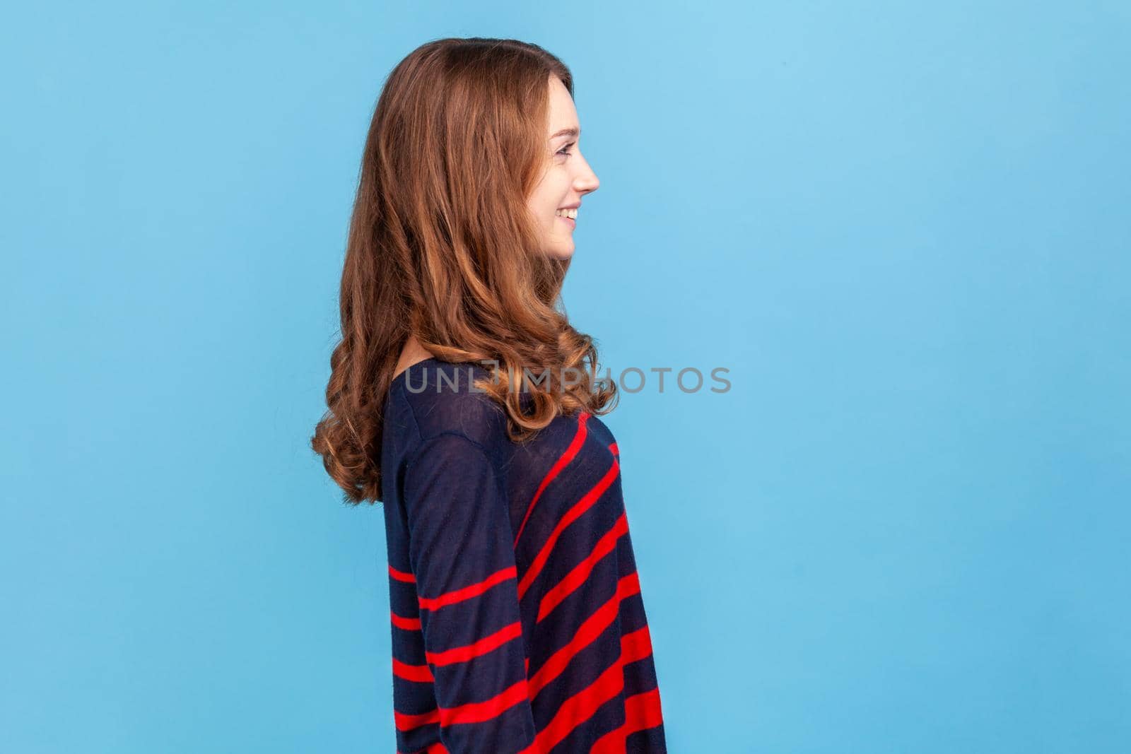 Side view of smiling woman wearing striped casual style sweater standing and looking ahead, having positive expression, being in good mood. by Khosro1