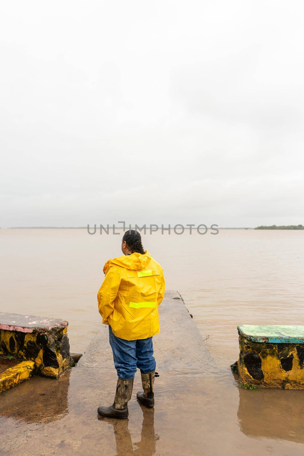 Vertical photo of a Latino mature man with long hair tied back and wearing a raincoat on a dock in Bluefields Nicaragua