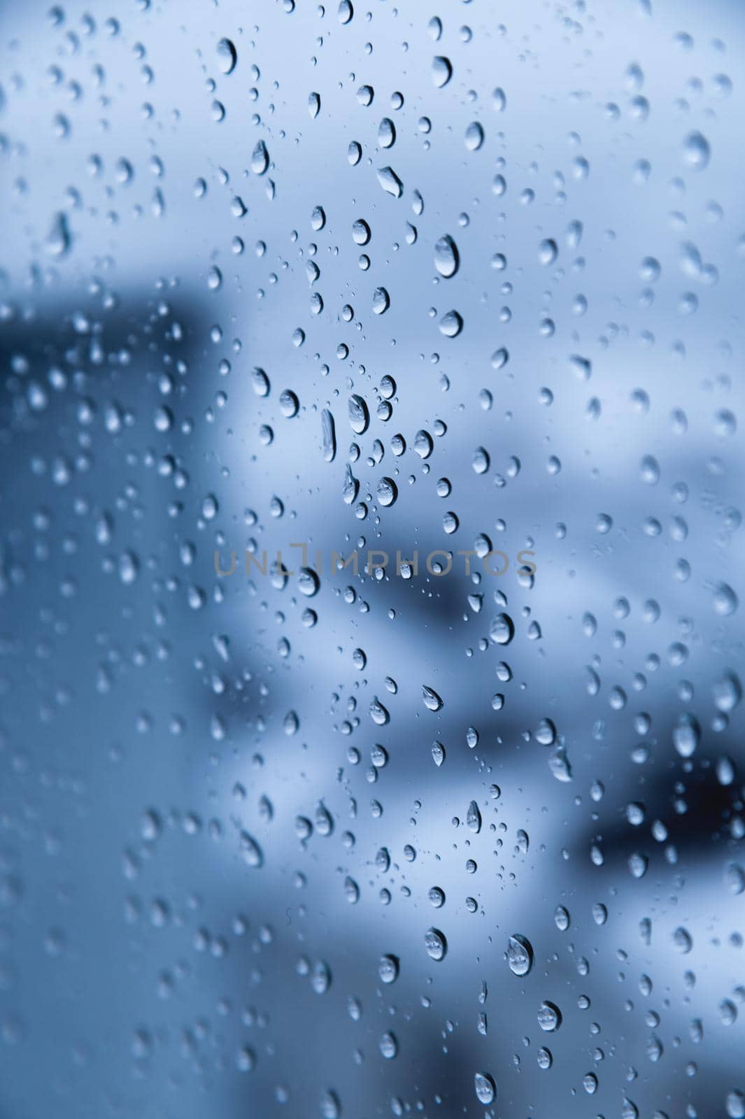 Drops of rain on blue glass with defocused streets. Urban abstract background by yanik88