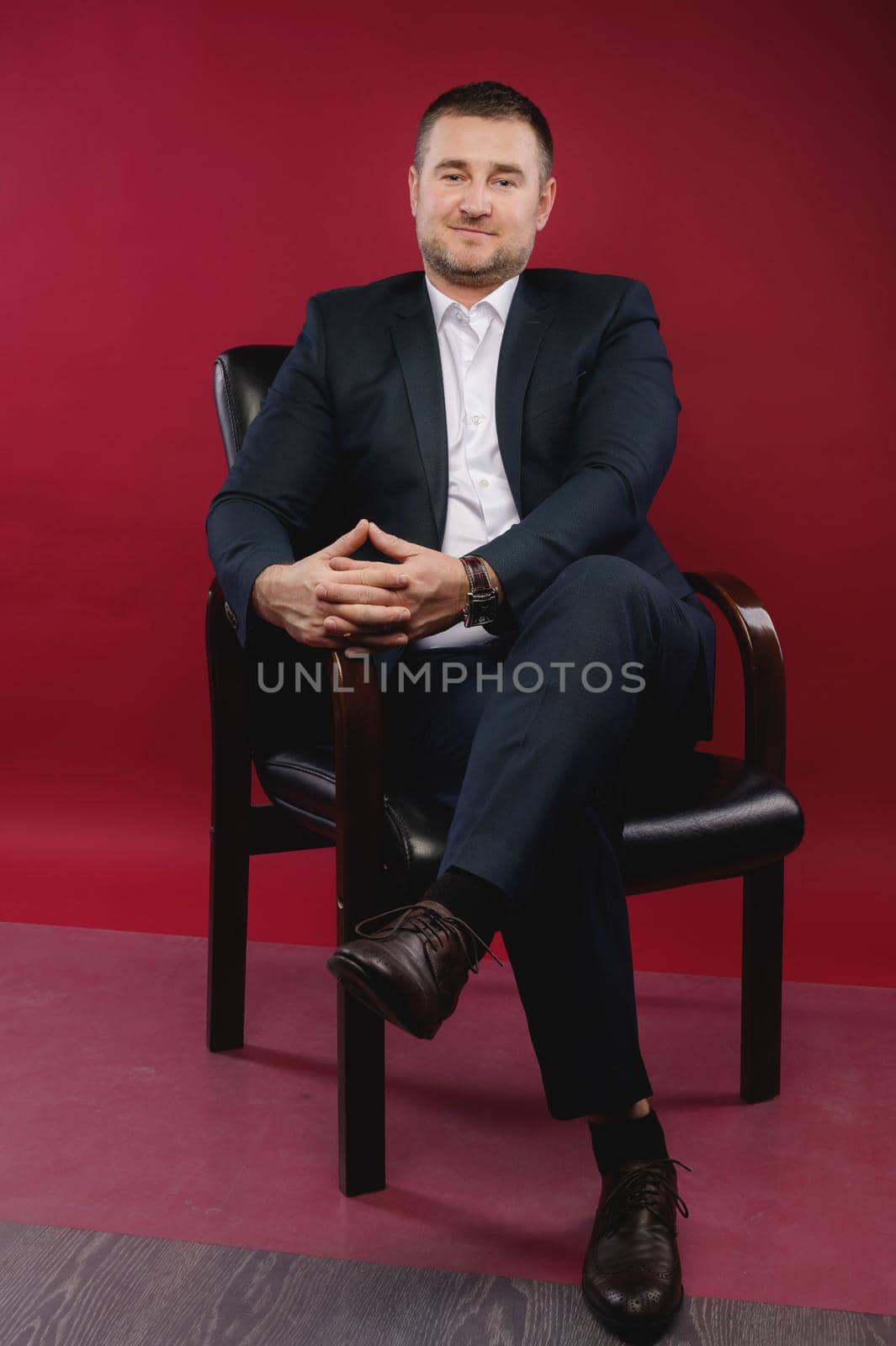 Portrait of a business man in a black suit sitting in a studio on a chair against an empty wall by yanik88