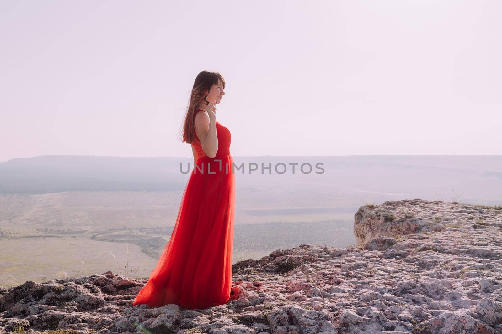 A girl in a red dress on the background of the mountains lifestyle. Illustrating articles about travel. A girl with a beautiful view. Vacation in Crimea. White rock. View of the villages. Lifestyle processing. Copy space .