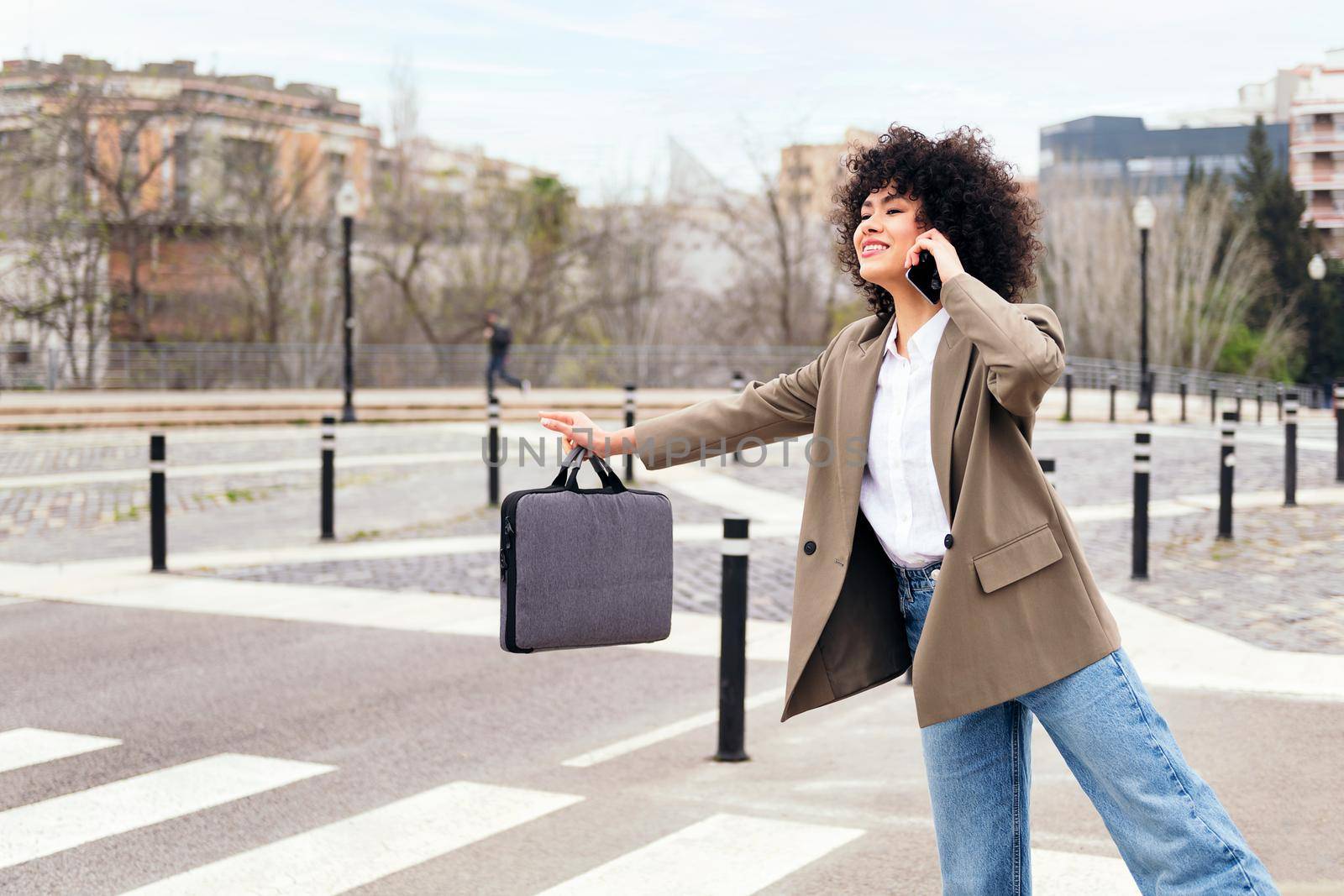 smiling young business woman talking on the phone while hailing a taxi, concept of communication and urban lifestyle, copy space for text