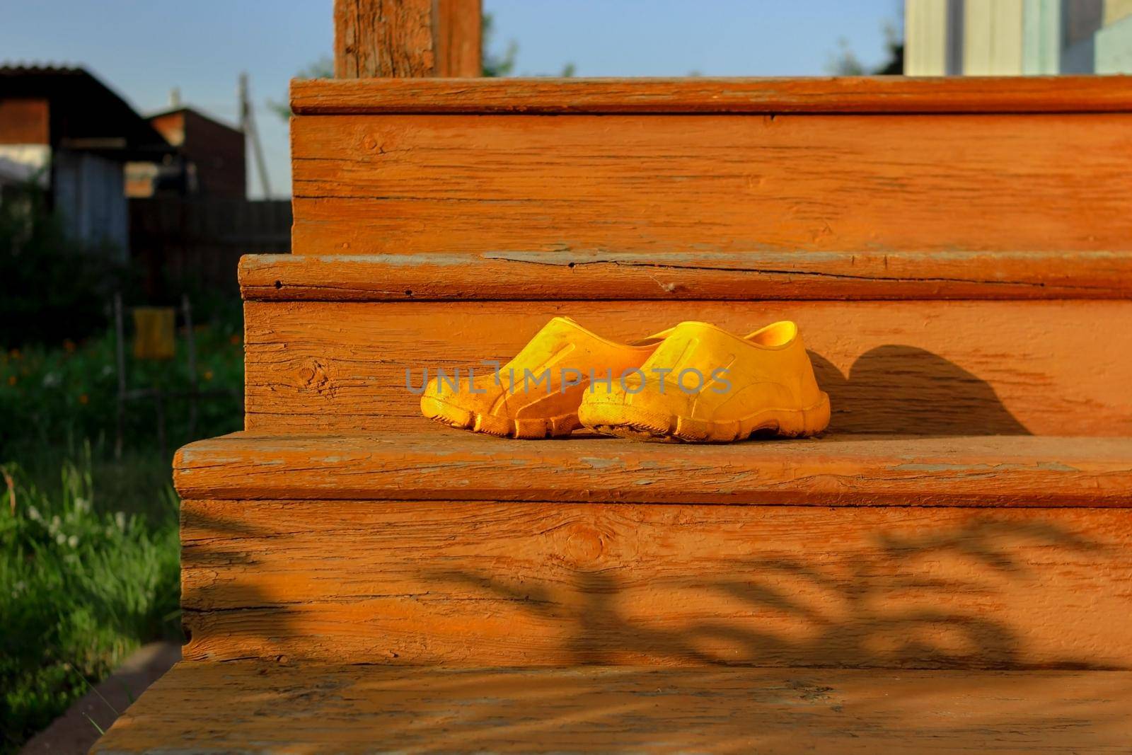 Yellow rubber muddy work shoes on old orange stairs on summer backyard at sunset, village and countryside authentic mood, low angle