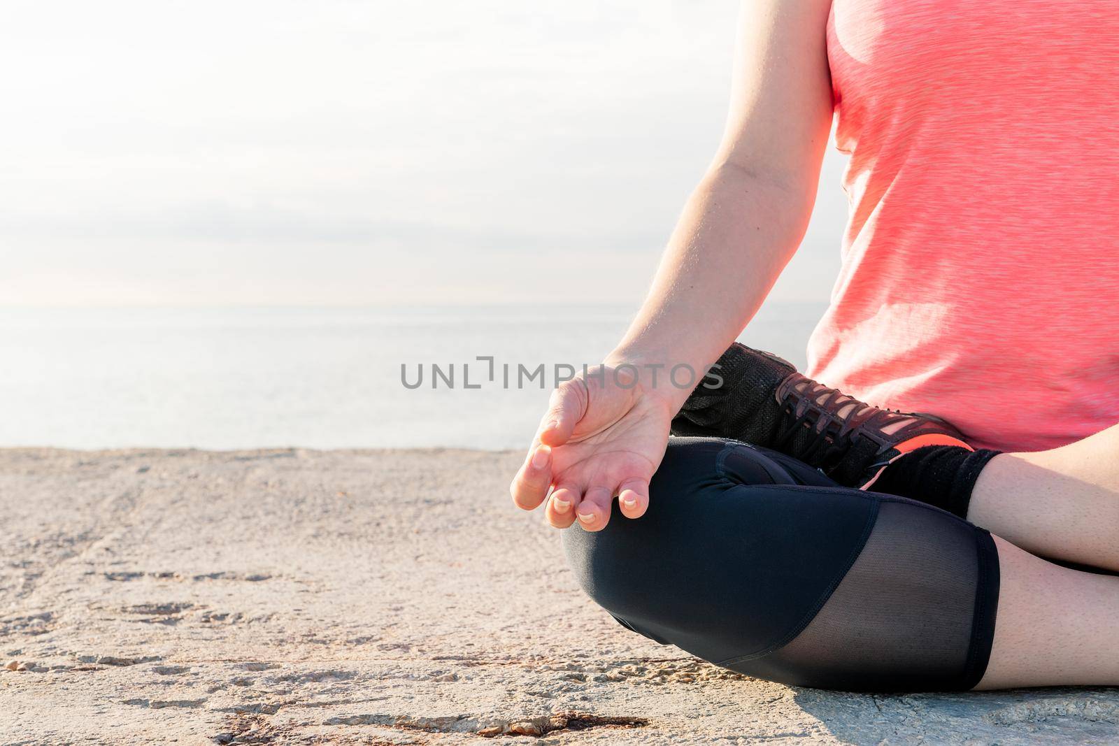 detail of the hand of an unrecognizable woman practicing yoga in the lotus position at dawn sitting in front of the sea, concept of mental health and relaxation, copy space for text