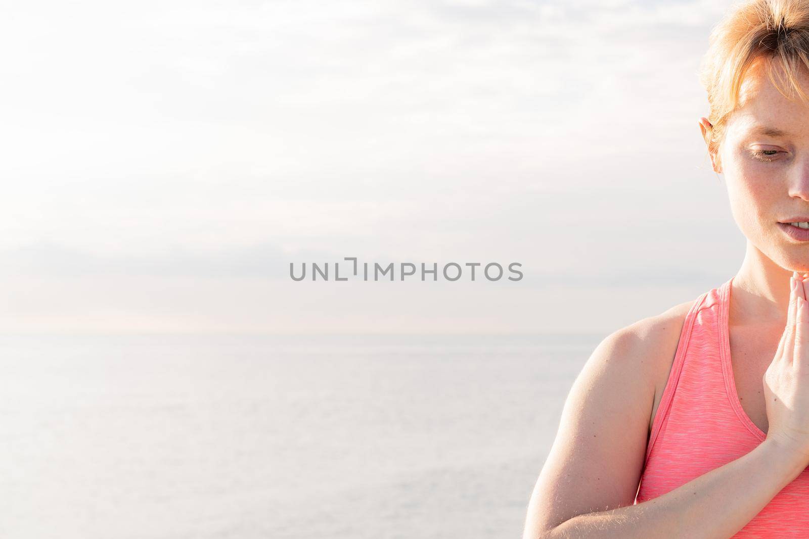 portrait of a blonde woman practicing yoga at dawn sitting in front of the sea, concept of mental health and relaxation, copy space for text
