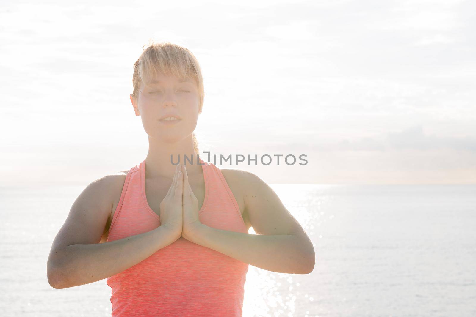 portrait of a blonde woman with her eyes closed practicing yoga at dawn in front of the sea, concept of mental health care and relaxation, copy space for text