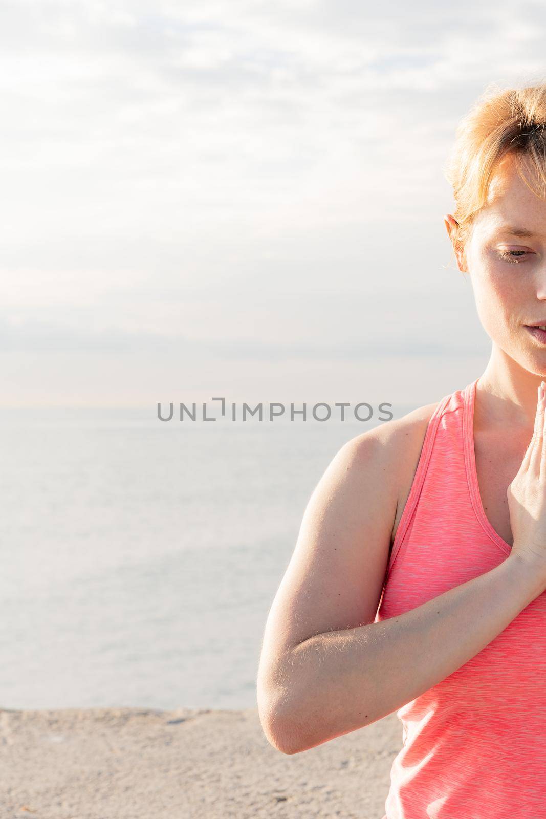 vertical portrait of a blonde woman practicing yoga at dawn sitting in front of the sea, concept of mental health and relaxation, copy space for text