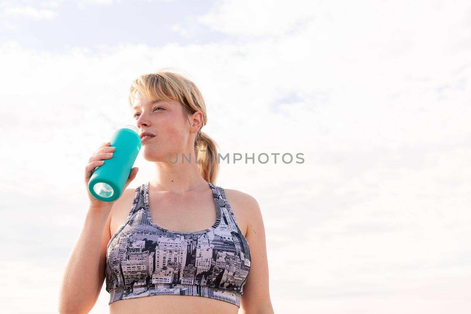 sportswoman with a bottle of water with the sky in the background, healthy lifestyle and sports concept, copy space for text