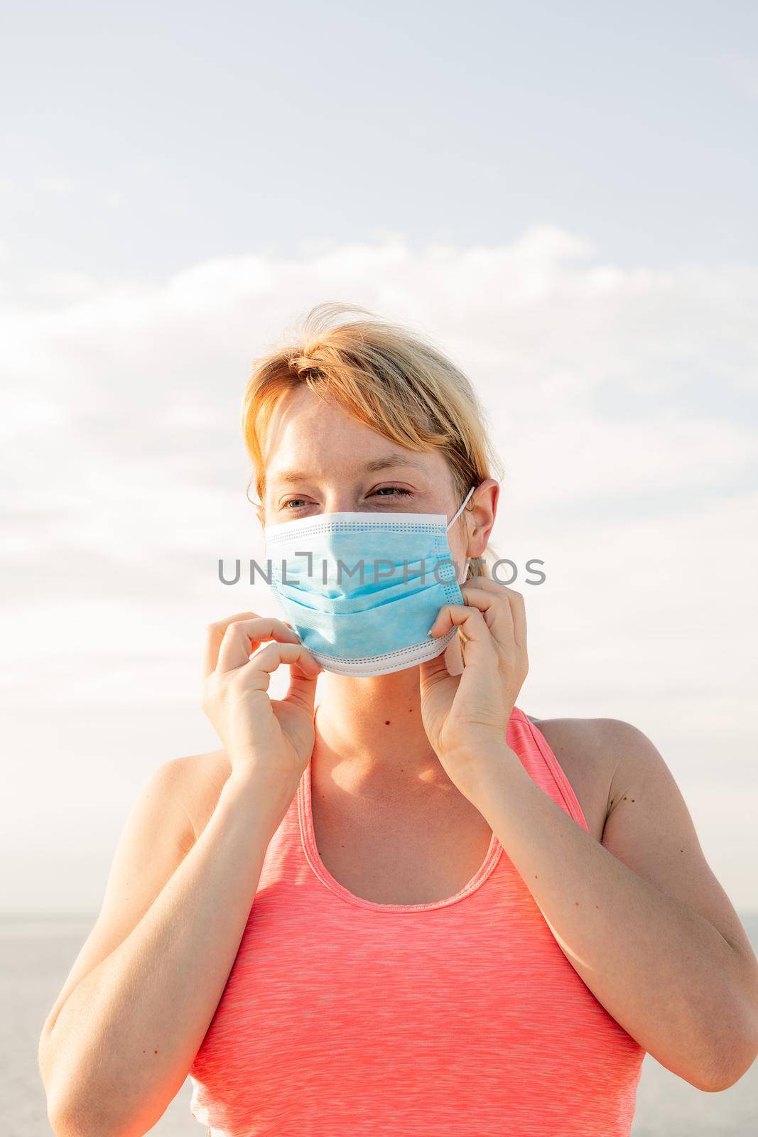 vertical portrait of a beautiful blonde woman wearing a protective mask with the sky in the background, concept of prevention and health care, copy space for text