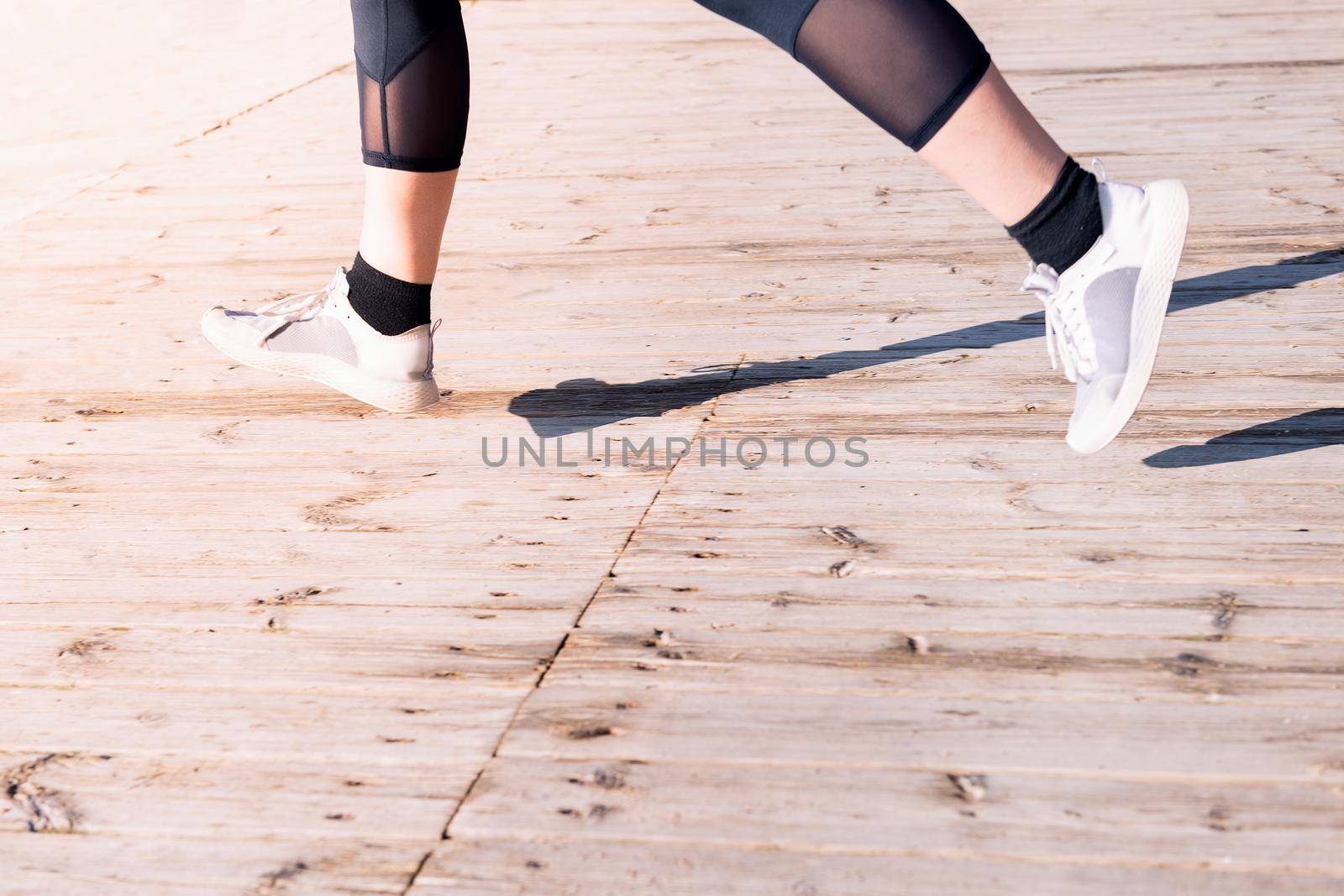 unrecognizable female runner's legs jogging in sneakers on a wooden floor, sport concept and healthy lifestyle, copy space for text