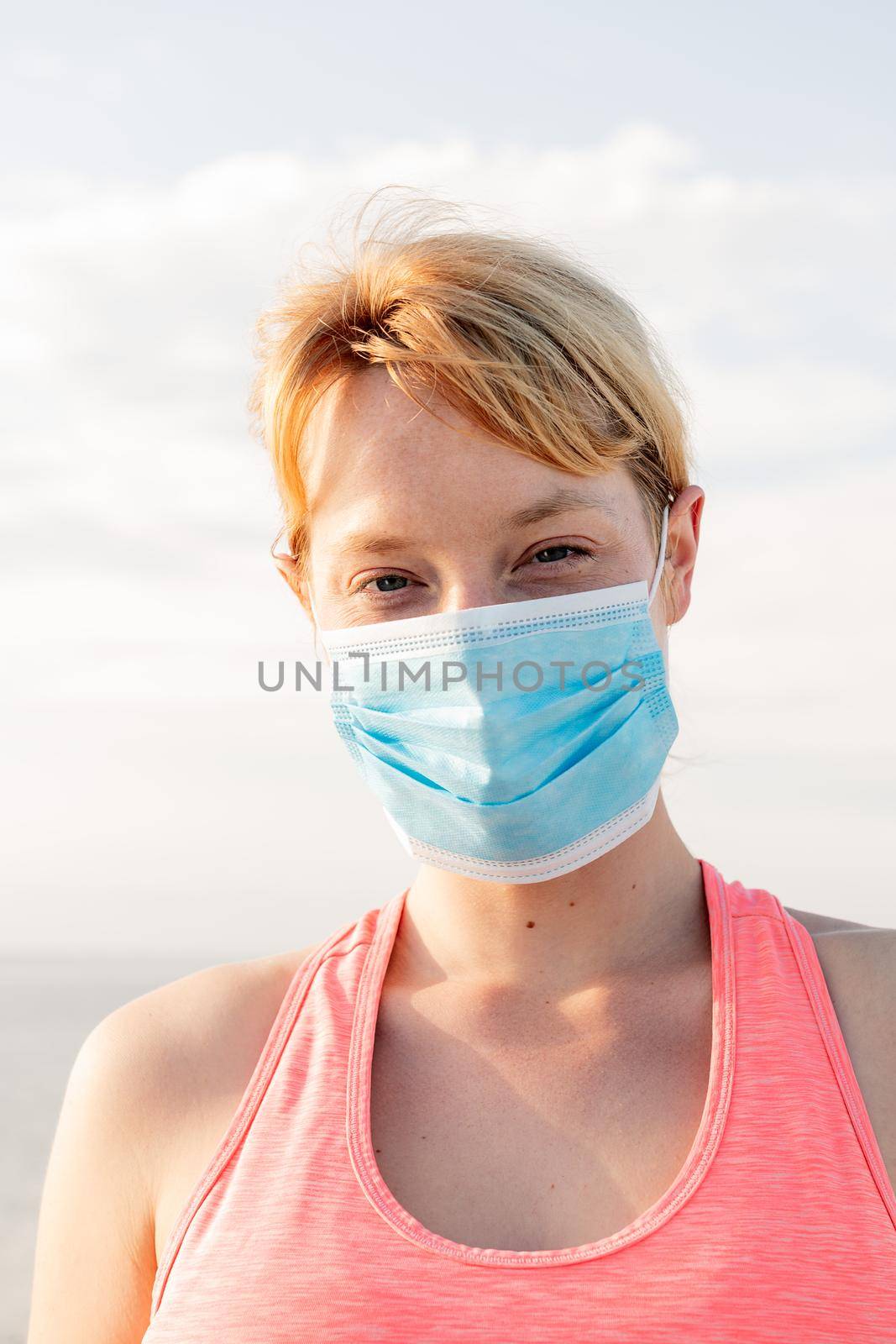 vertical portrait of a beautiful blonde woman with a protective mask with the sky in the background, concept of prevention and health care