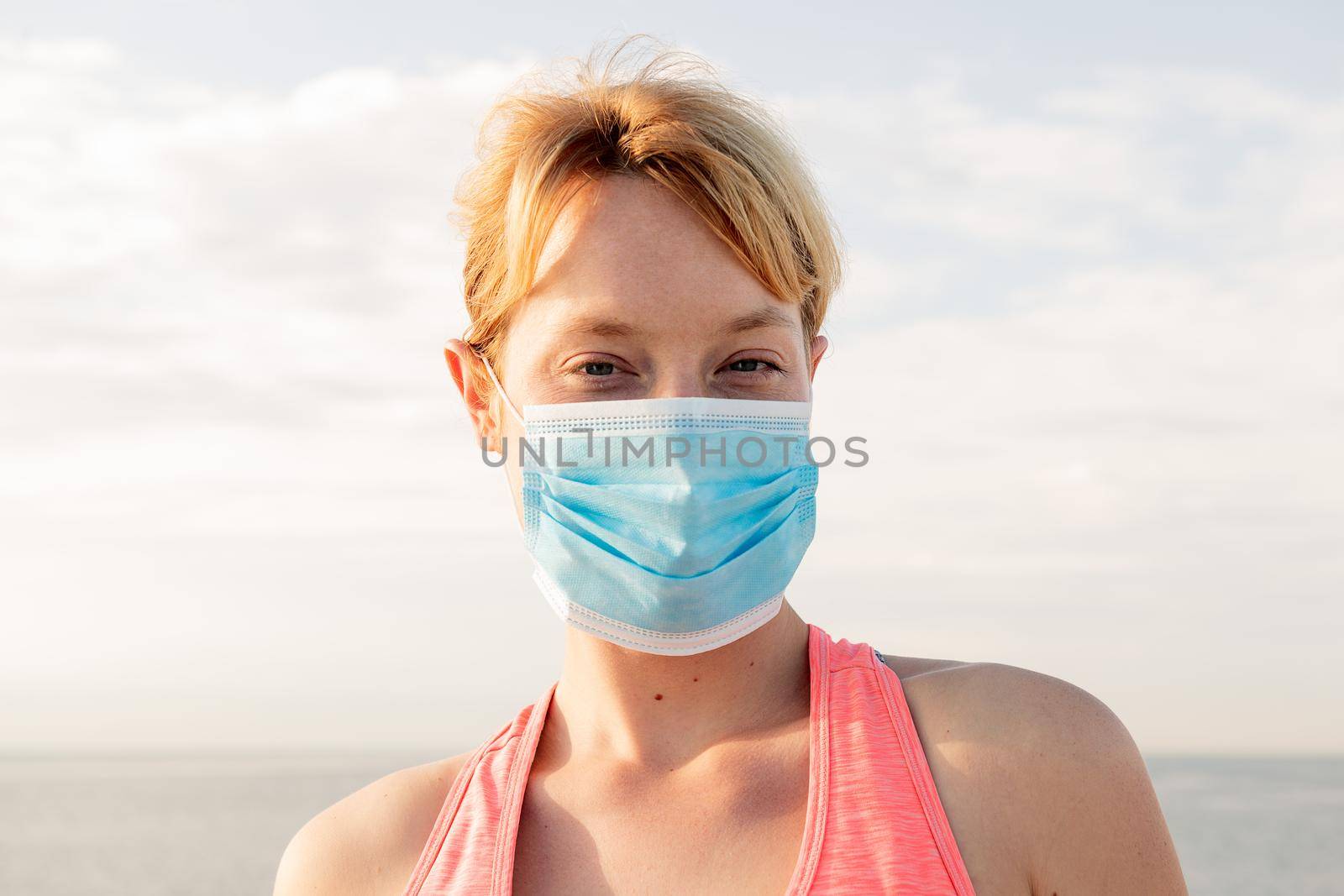 portrait of a beautiful blonde woman with a protective mask with the sky in the background, concept of prevention and health care