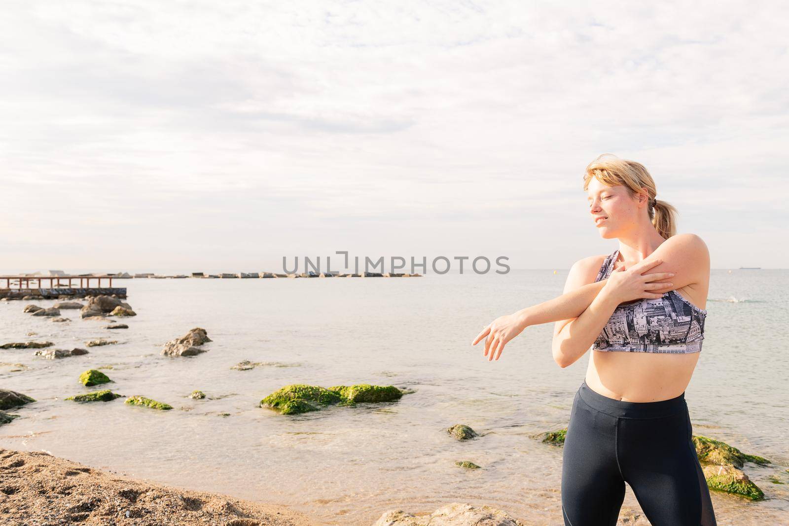 beautiful sporty woman stretching in front of the sea at dawn, healthy lifestyle and sport concept, text copy space