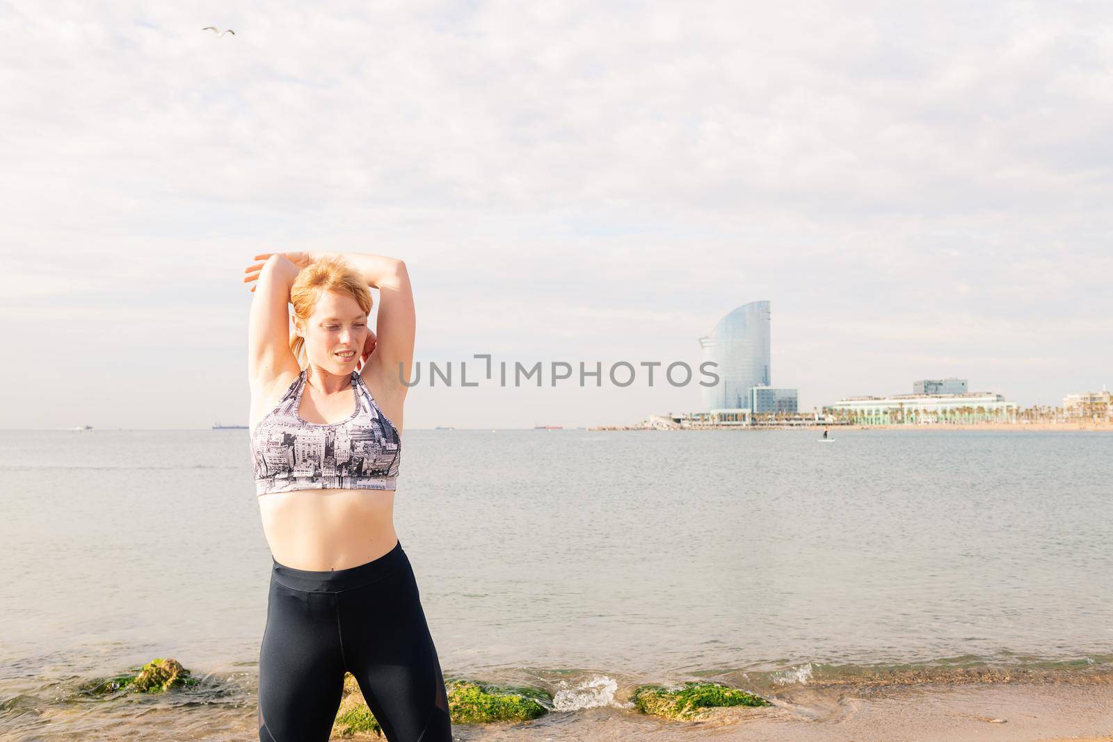 beautiful sporty woman stretching out in front of the sea in the city, healthy lifestyle and sport concept, copy space for text
