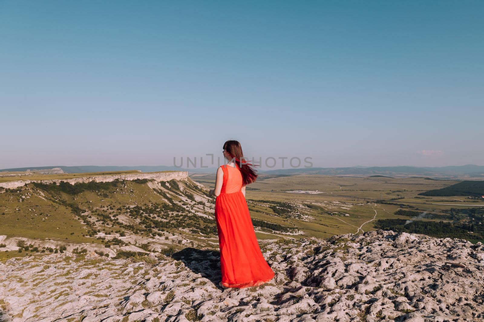 A girl in a red dress on the background of the mountains lifestyle. Illustrating articles about travel. A girl with a beautiful view. Vacation in Crimea. White rock. View of the villages. Lifestyle processing. Copy space .