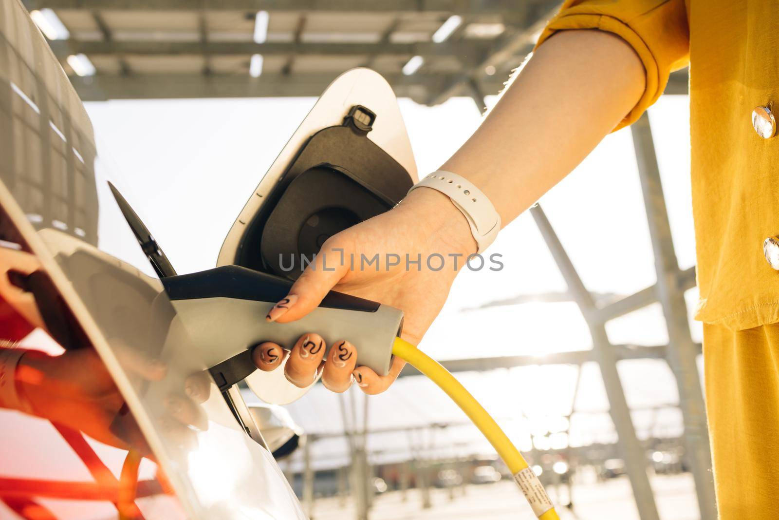 Woman hand inserts power cable supply to charge electric or EV car. Female plugging an electric car or EV at electric charging station.