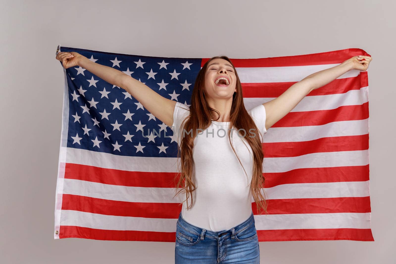 Beautiful young woman with dark hair, holding USA flag over shoulders, rejoicing happily. by Khosro1