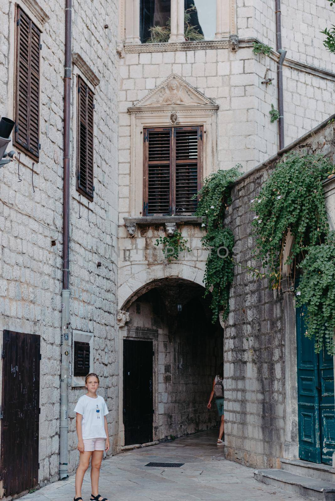 Girl Tourist Walking Through Ancient Narrow Street On A Beautiful Summer Day In MEDITERRANEAN MEDIEVAL CITY, OLD TOWN KOTOR, MONTENEGRO. Young Beautiful Cheerful Woman Walking On Old Street. Europe by Andrii_Ko