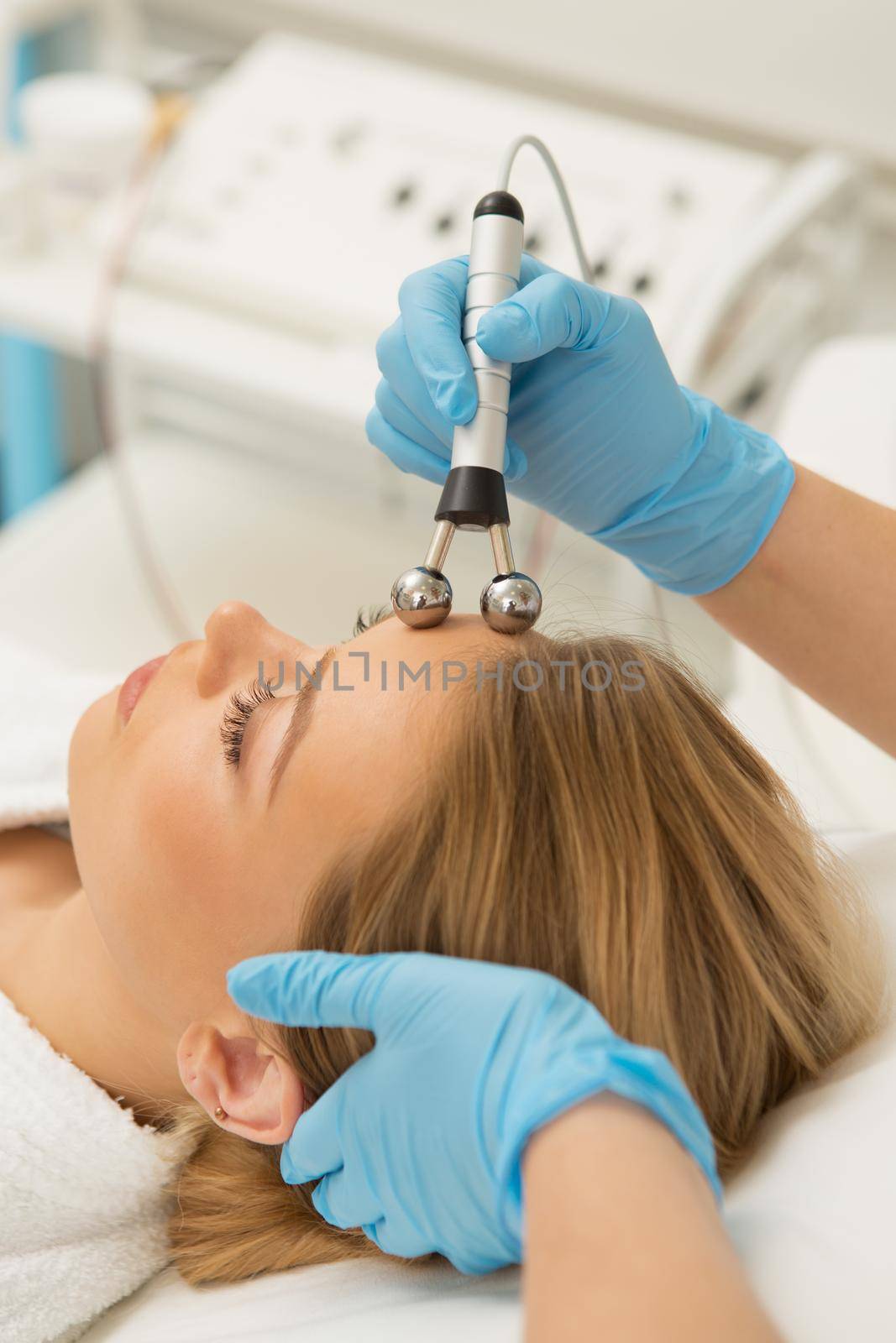 Vertical shot of a professional cosmetologist working with her client performing skin tightening microcurrent treatment for her female client beauty skincare youth rejuvenation wellness stimulating