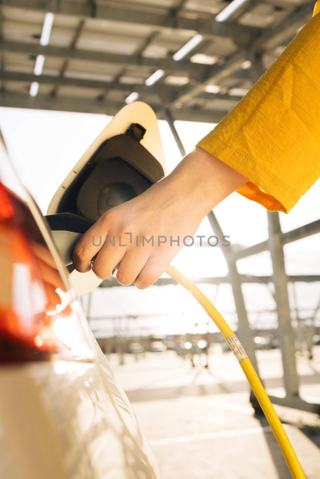 Woman hands attaching power cable supply to charge electric or EV car on the solar panels background. Female plugging an electric car or EV at electric charging station by uflypro