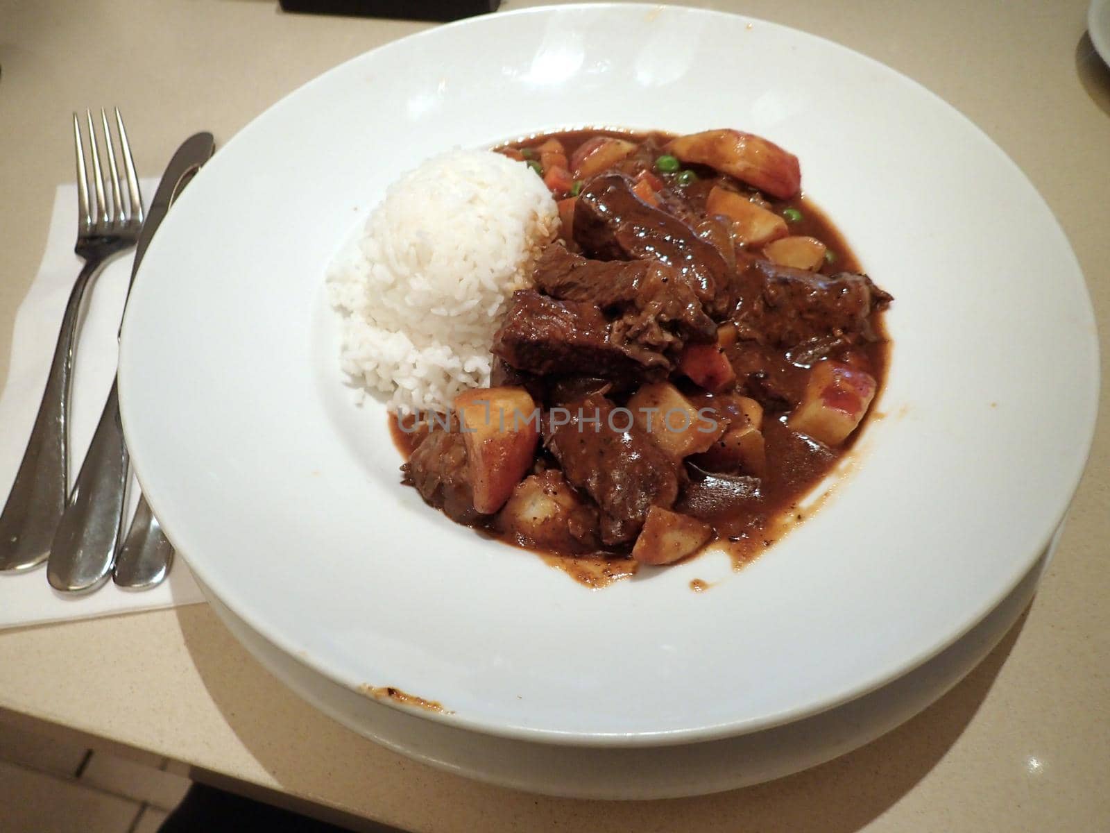 Hawaiian style Beef Stew with carrots, potatos, peas with rice bowl plate on table.