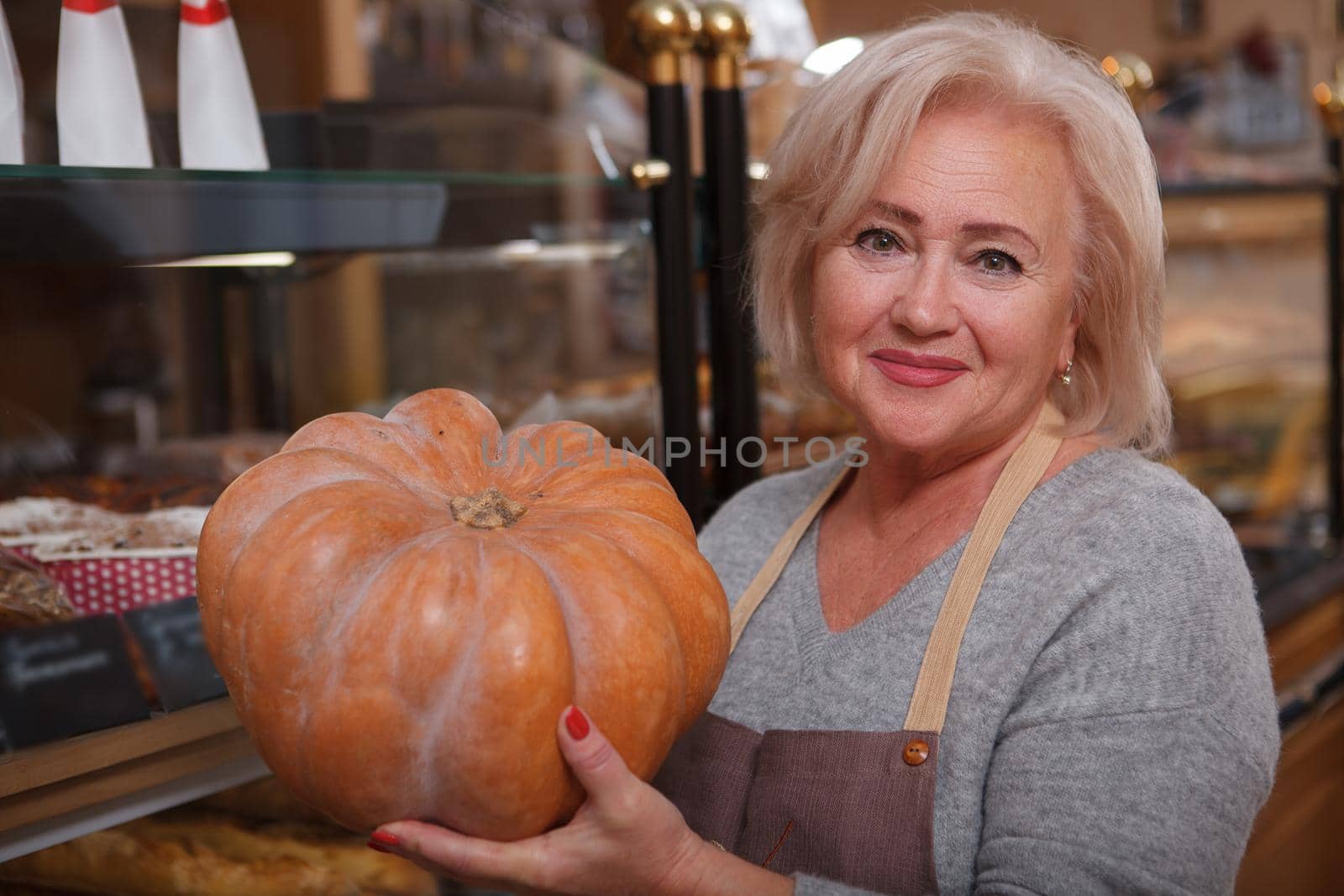 Happy senior woman holding a pumpkin enjoying working at her small groceries store