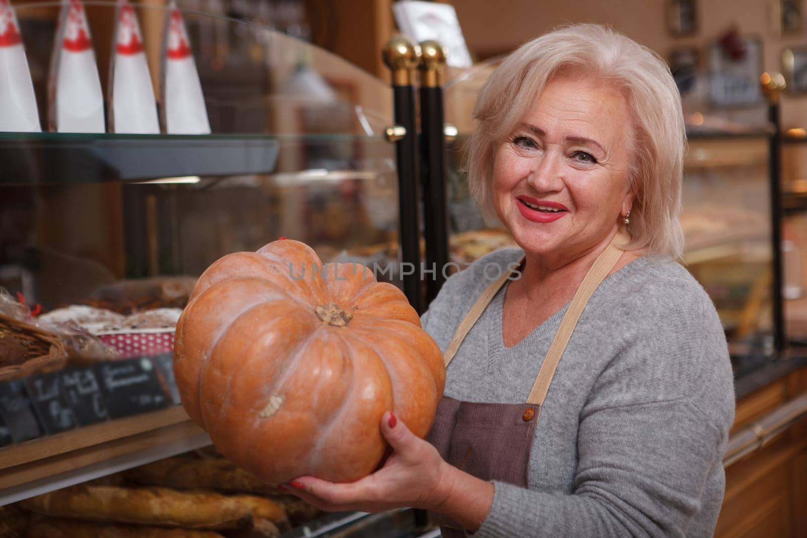 Happy senior female shop assistant laughing joyfully holding a pumpkin working at her store