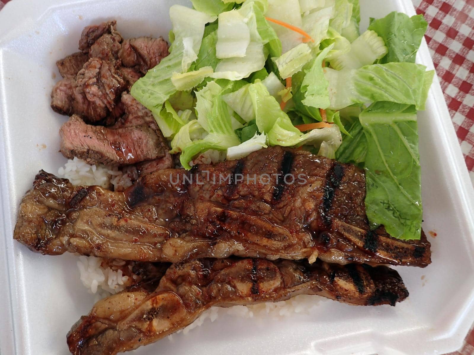 Steak, Kalbi, Side salad and white rice in a styrofoam plate.