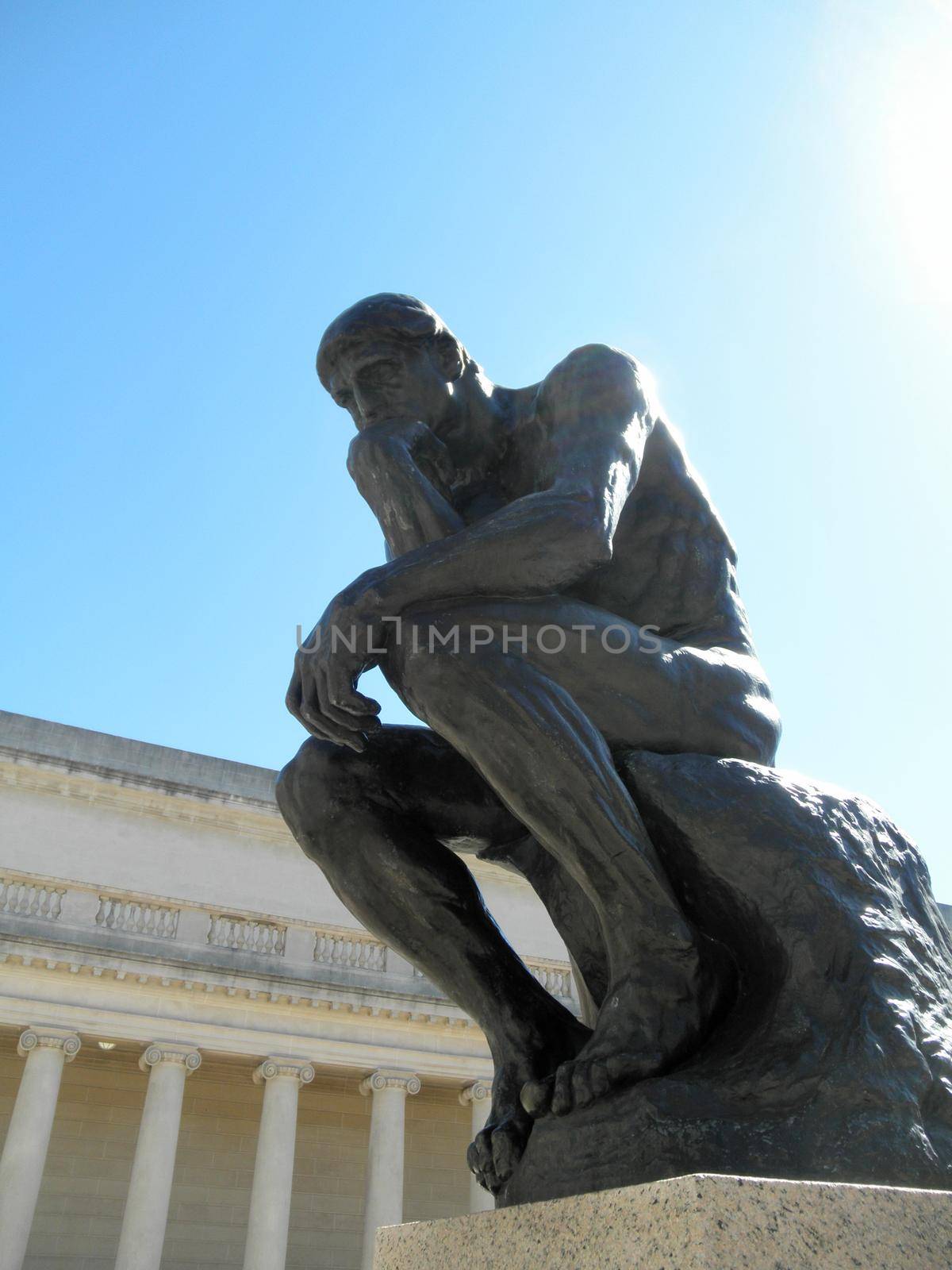 Side front profile of the masterpiece the Thinker by Rodin - The Thinker at the entrance of the Palace of the Legion of Honor in San Francisco with sunlight shinning down at it.      