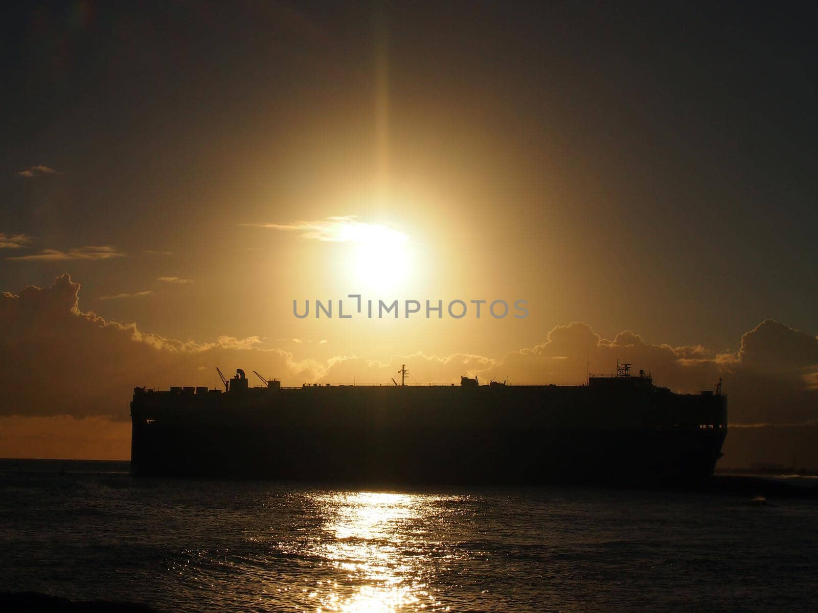 Dramatic Sunset over Pacific Ocean with Cargo Ship passing through the water off the coast of  Oahu, Hawaii.