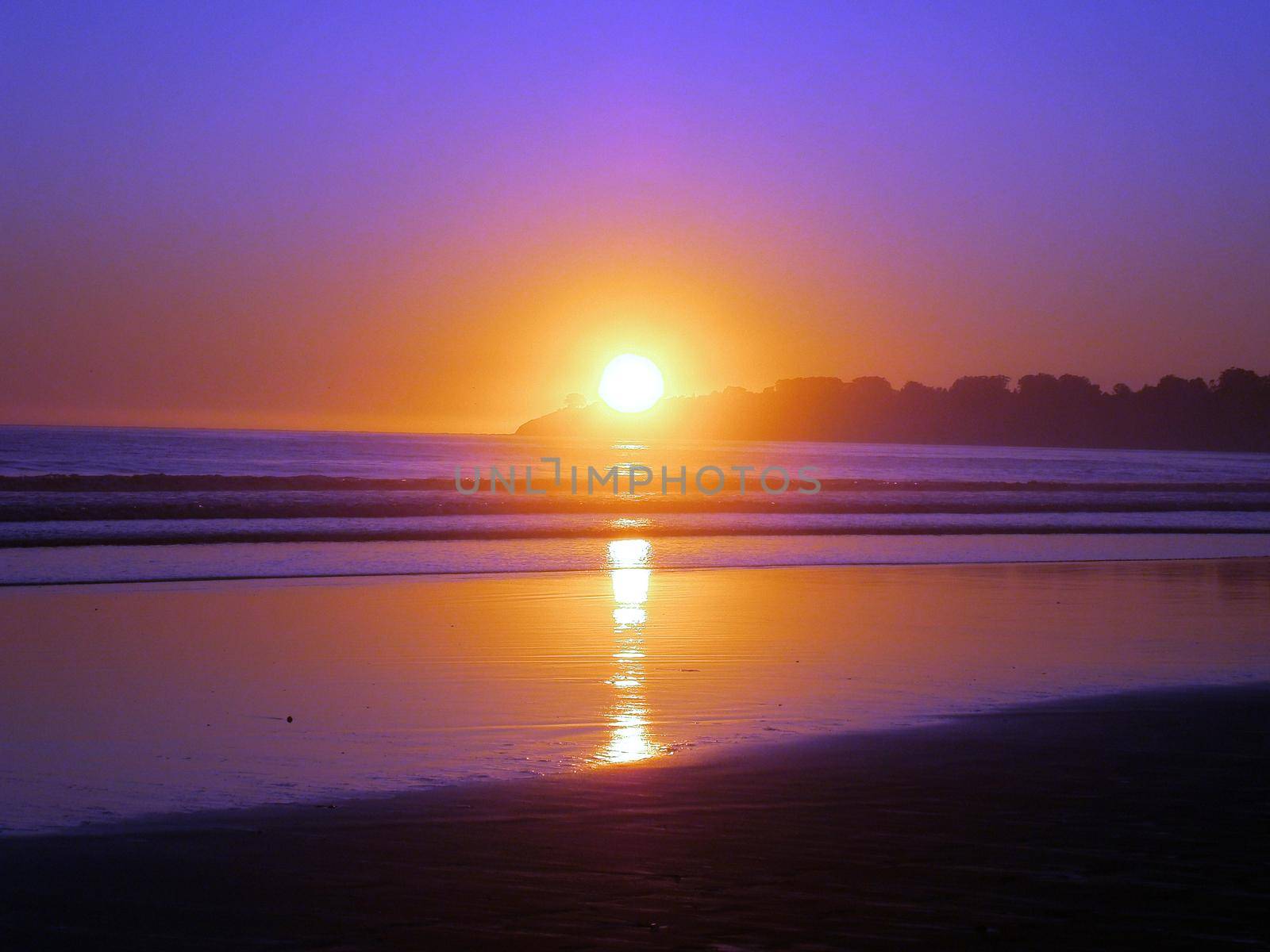 Epic sunset reflects on ocean and beach on an empty clear sky day behind hill at Stinson Beach, California.