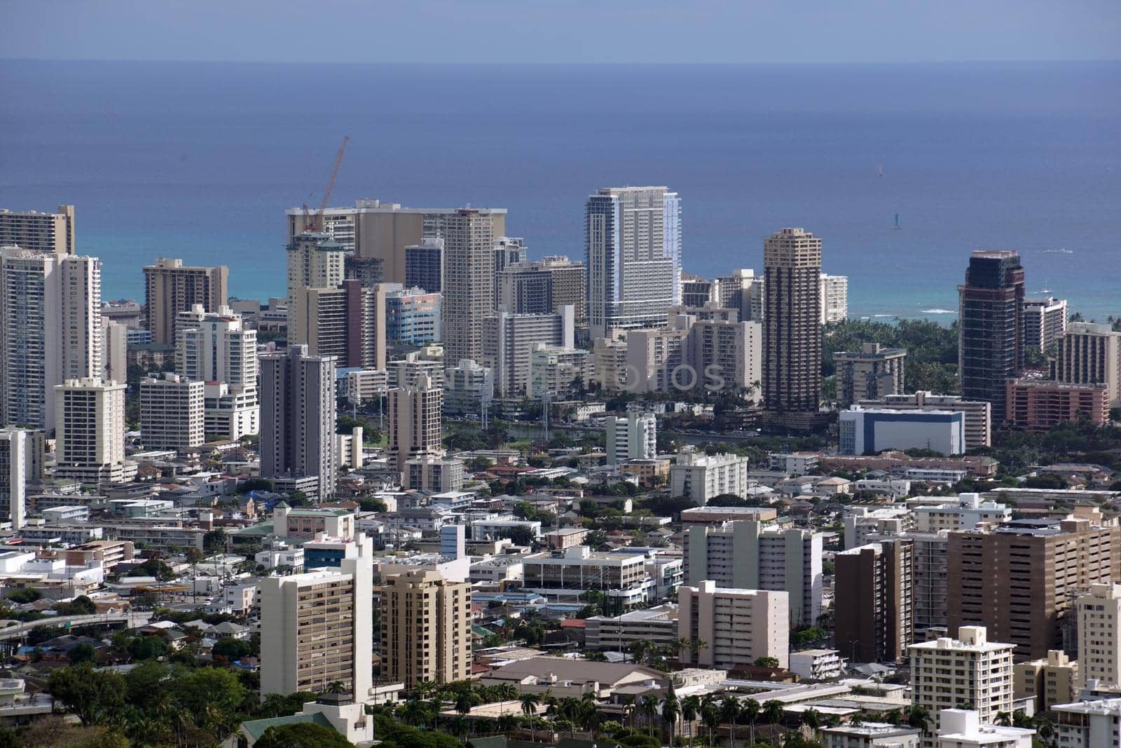 Honolulu cityscape, roads, buildings, skyscrapers, cranes, parks, and Pacific Ocean with clouds in the sky seen from up in the mountains on Oahu, Hawaii. 