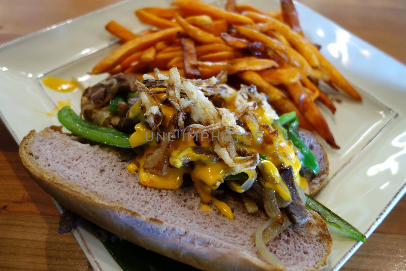 Pipikaula Cheese Steak with Sweet Potato fries - Classic dried beef seared with green peppers and onions topped with our house-made nacho cheese and crispy onion garnish and Sweet Potato fries on the side.