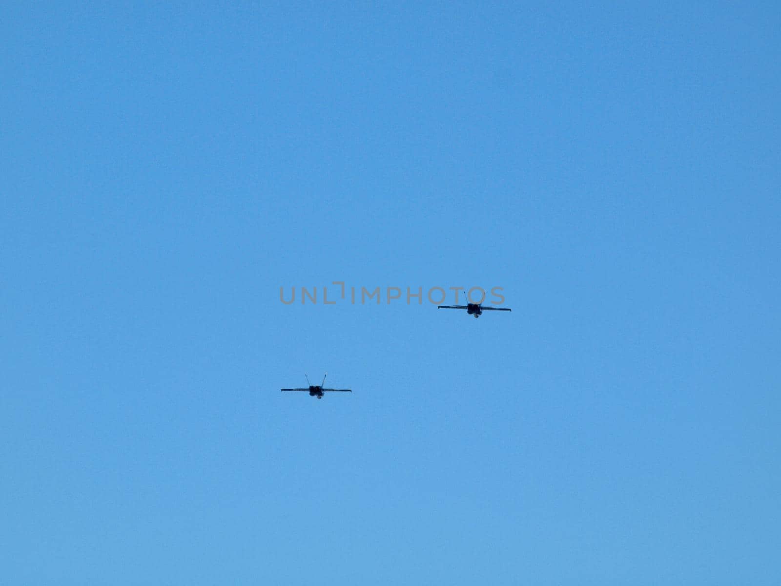 Two Fighter Jets fly in the air in a blue sky.